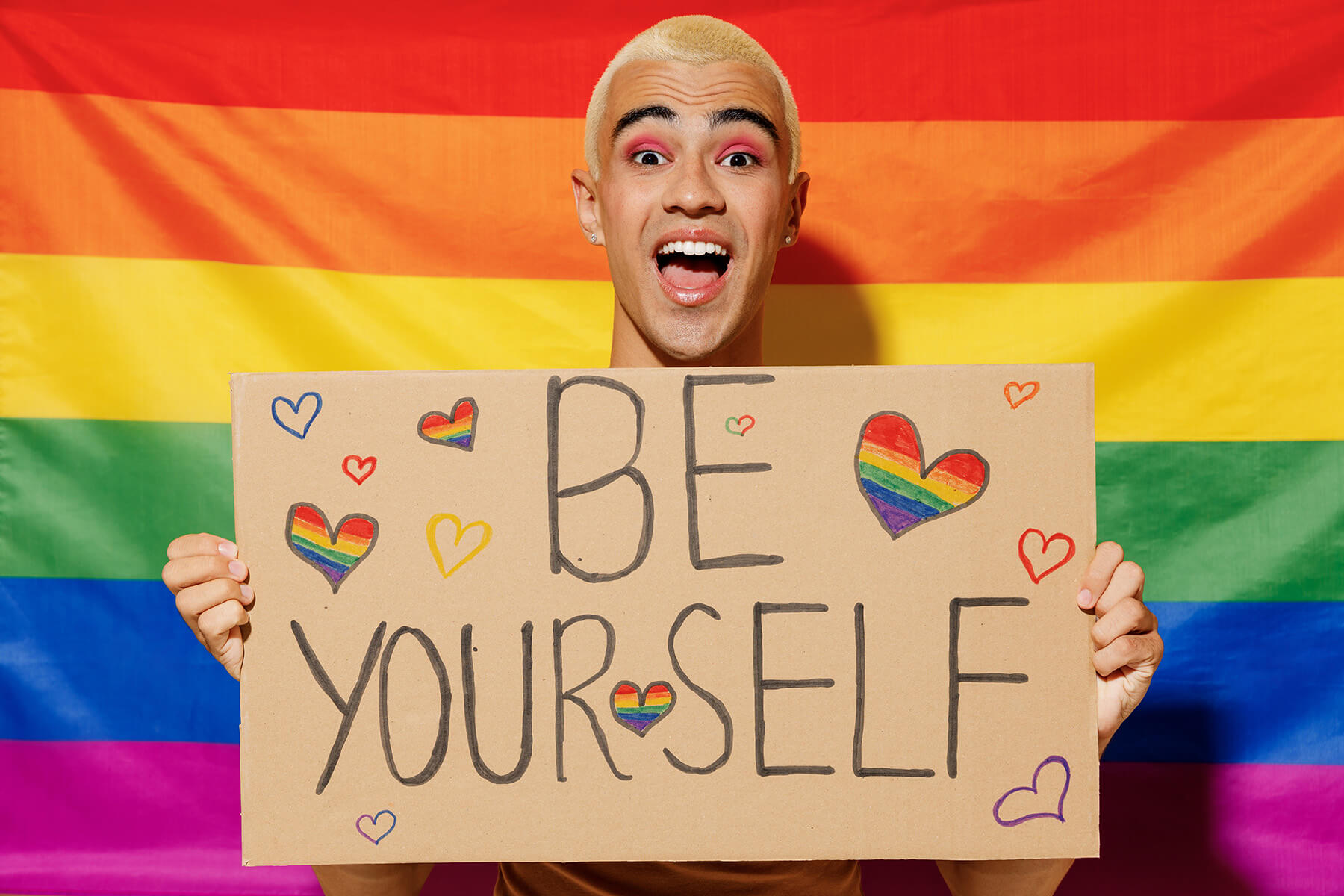 Queer person holding a sign that says "be yourself"